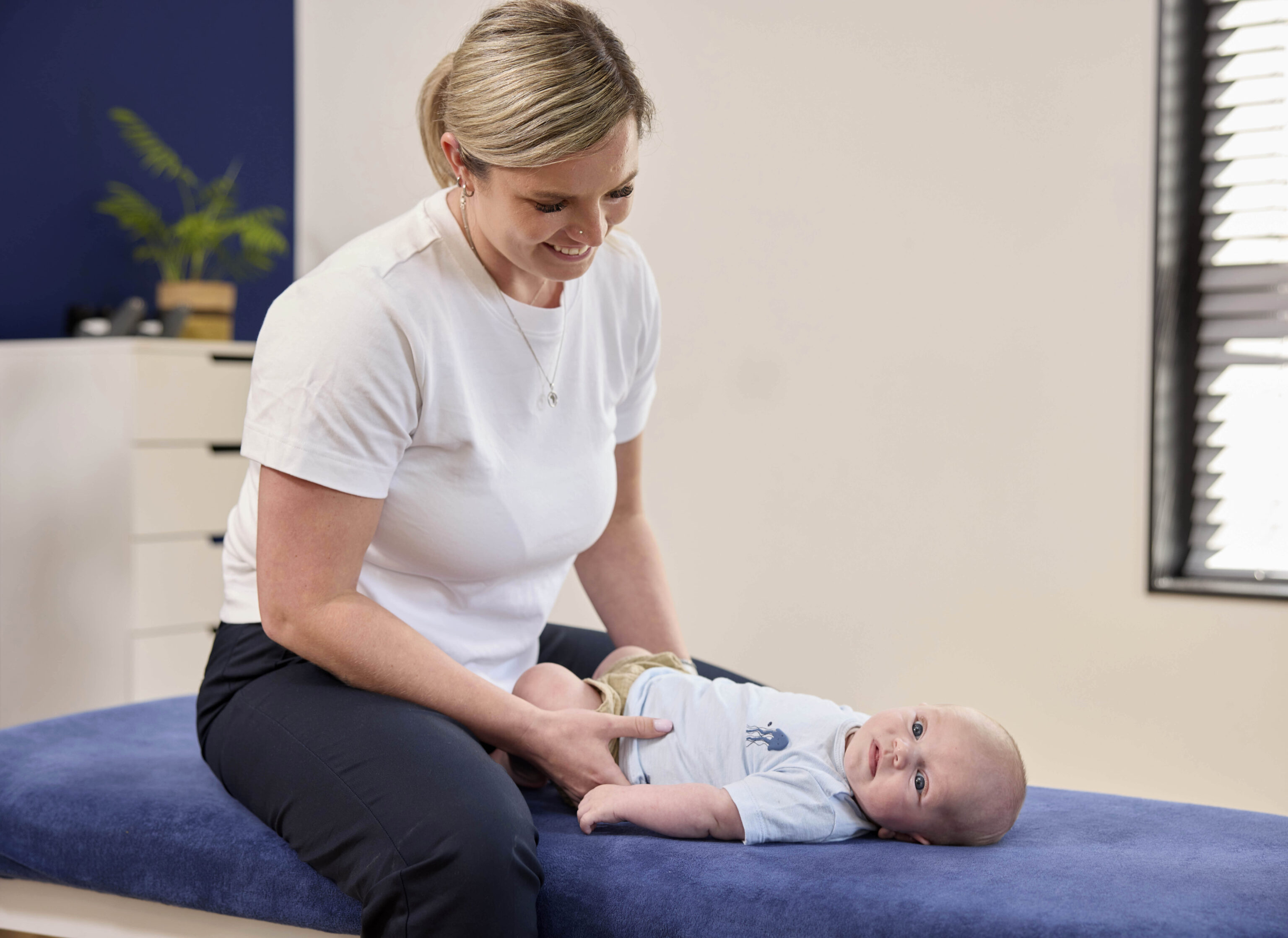 Vrouwelijke chiropractor lacht naar baby op behandeltafel